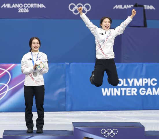 한국 여자 쇼트트랙 대표팀 김길리(오른쪽)이 21일 이탈리아 밀라노 아이스스케이팅 아레나에서 열린 2026 밀라노·코르티나 동계올림픽 쇼트트랙 여자 1500m에서 우승한 뒤 시상대에서 펄쩍 뛰어오르며 기뻐하고 있다. 은메달리스트인 선배 최민정이 김길리를 향해 박수치고 있다. 김길리는 이번 대회에서 금메달 2개, 동메달 1개를 따냈다. 연합뉴스
