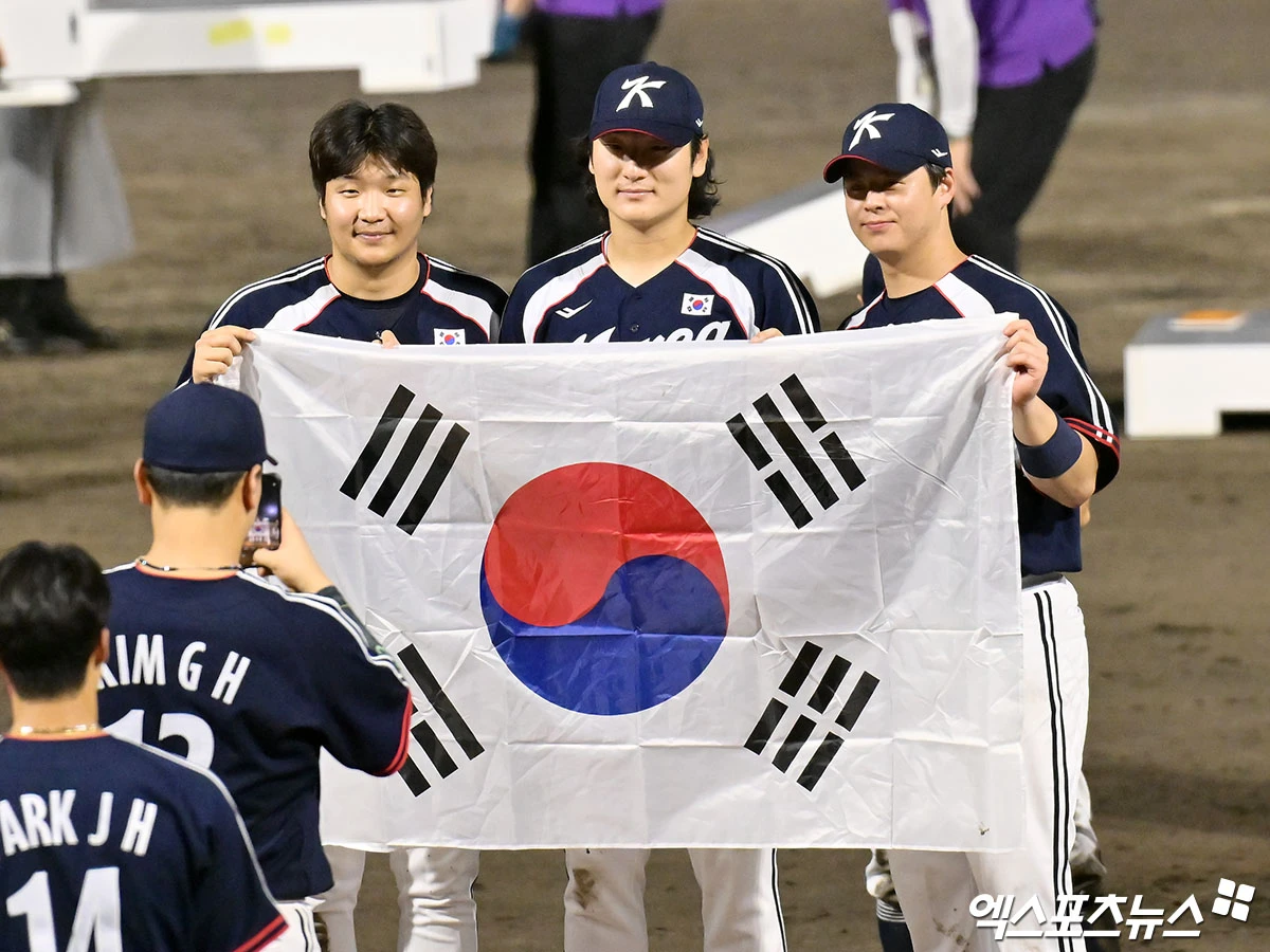 야구대표팀 주장 노시환(오른쪽)이 지난 27일 일본 아이치현 도요하시 시민구장에서 열린 2026 아이치·나고야 아시안게임 금메달 결정전에서 일본을 3-1로 꺾고 금메달이 확정된 뒤 태극기를 들고 기념 촬영을 하는 모습. 사진 김한준 기자
